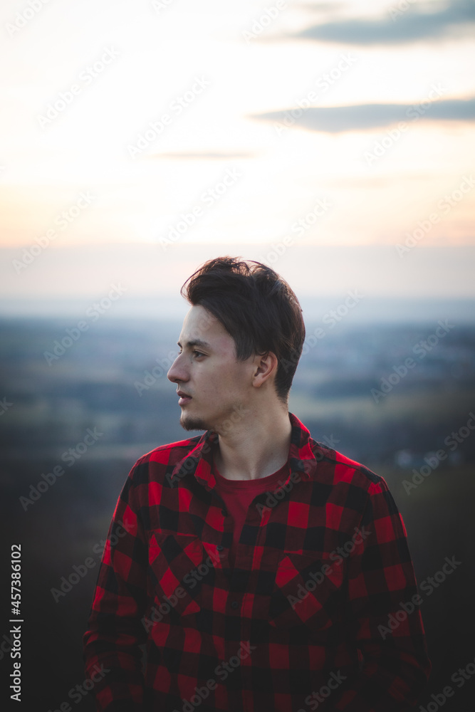 Candid portrait of a man in his 20s dressed in a black and red checked shirt looking into his future, immersed in his thoughts and contemplating. Authentic mood of a young man on an indecisive journey