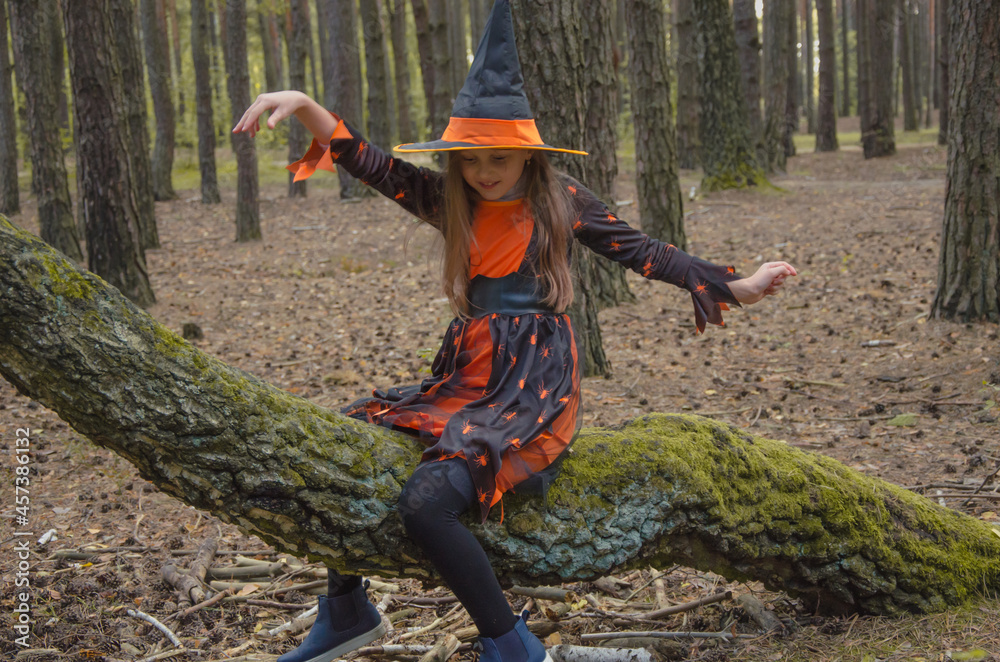 Naklejka premium a cute girl in a witch costume with a hat and cap sits on a tree like on a broomstick. halloween party