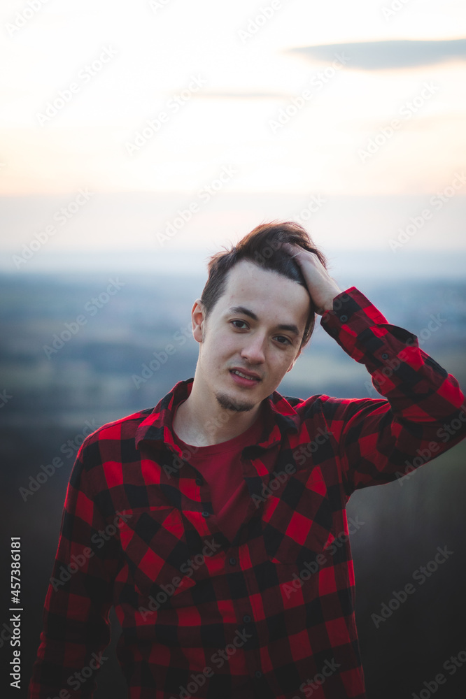 Candid portrait of a man in his 20s dressed in a black and red checked shirt looking into his future, immersed in his thoughts and contemplating. Authentic mood of a young man on an indecisive journey