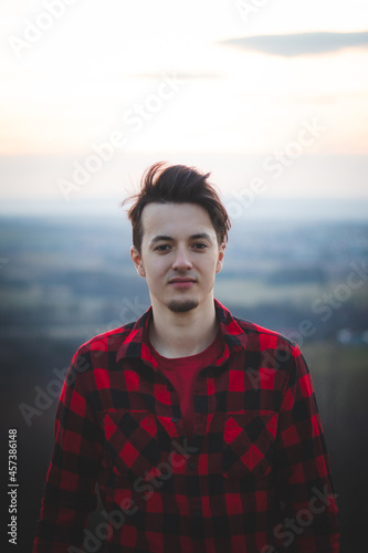 portrait of a twenty-three year old man in a black and red checked shirt, smiling at his friend with his real smile without any pretence. The authentic mood of a young man on an indecisive journey