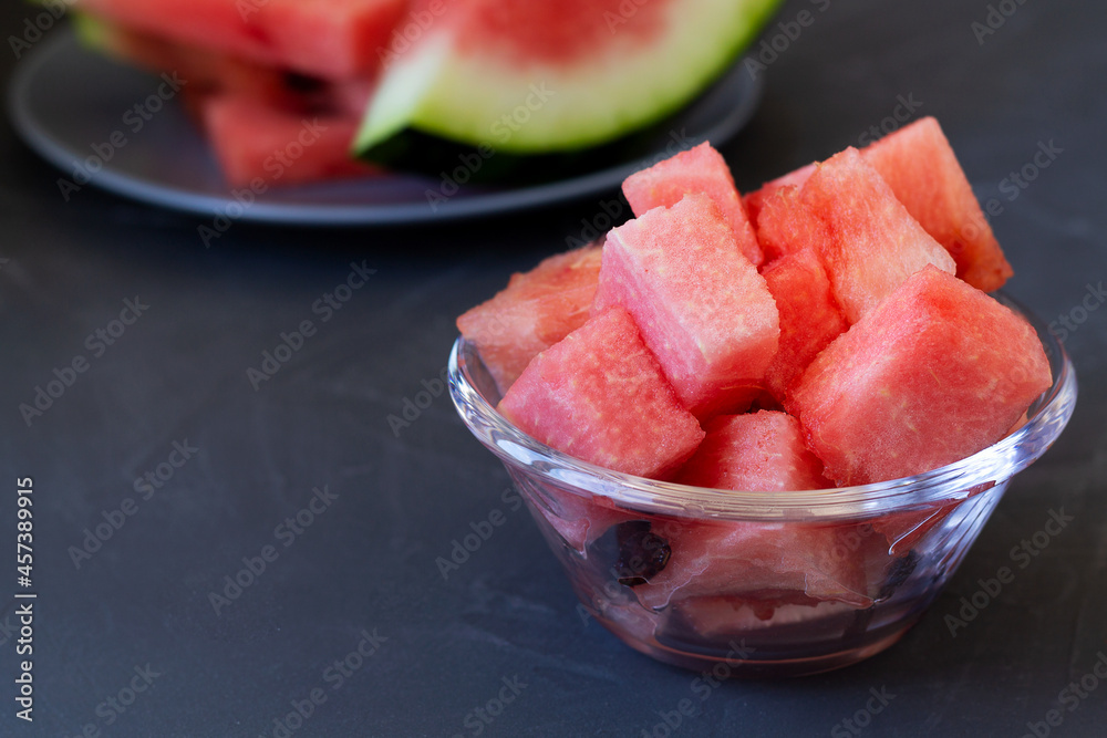 slices of red watermelon in a glass bowl on the black background. fresh watermelon on the grey plate on the table with copy space slices of red watermelon in a glass bowl on the black background. fresh watermelon on the grey plate on the table with copy space