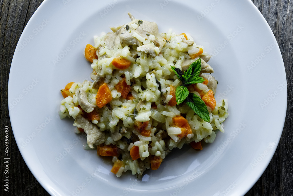 Top view of risotto with chicken, carrots and green basil on a white plate Top view of risotto with chicken, carrots and green basil on a white plate