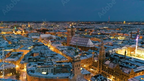 Munich aerial at night city covered with snow winer ambience, munich germany skyline drone video in 4k. Fly over marienplatz town hall and frauenkirche church.