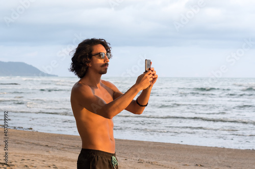 Man taking picture with phone at beach during sunset photo