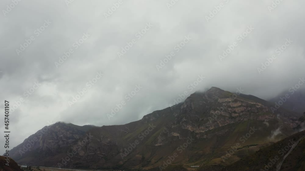 View from quadcopter of steep rocky mountains tops are covered with thick clouds