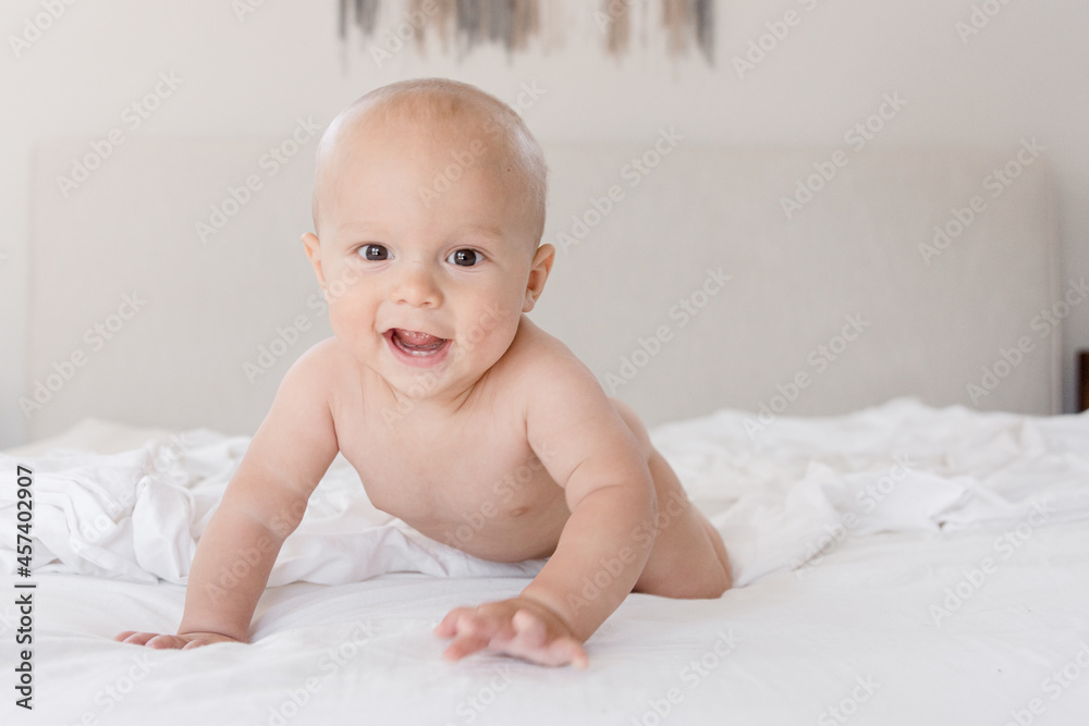 Infant smiling and looking at camera while crawling on white sheets Infant smiling and looking at camera while crawling on white sheets