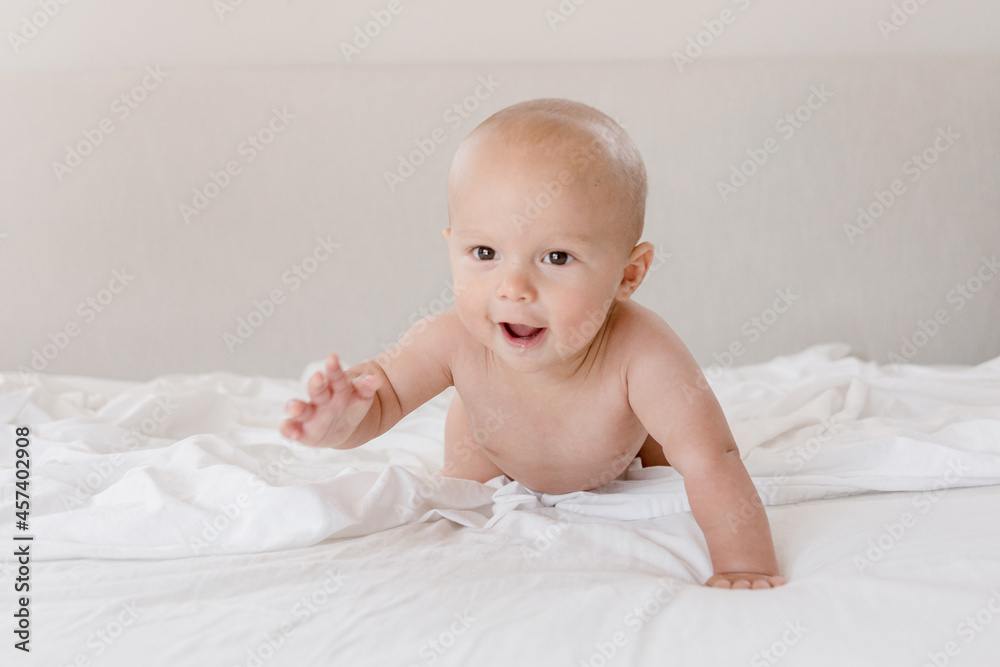 Crawling infant smiling while crawling on bed with white sheets Crawling infant smiling while crawling on bed with white sheets