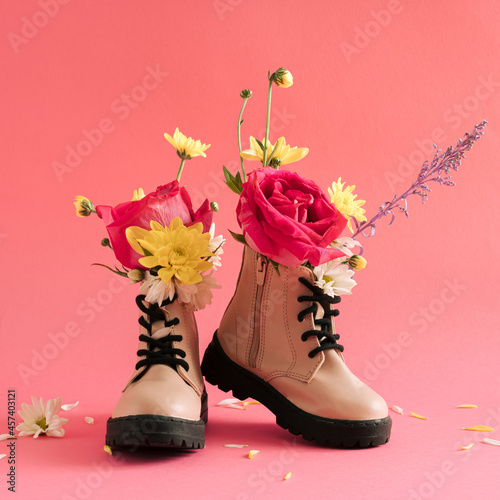 Creative layout with children's boots with various spring flowers on a pastel pink background. Minimal lifestyle concept.