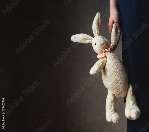 Cropped image of child's hand holding stuffed rabbit against dark wall photo