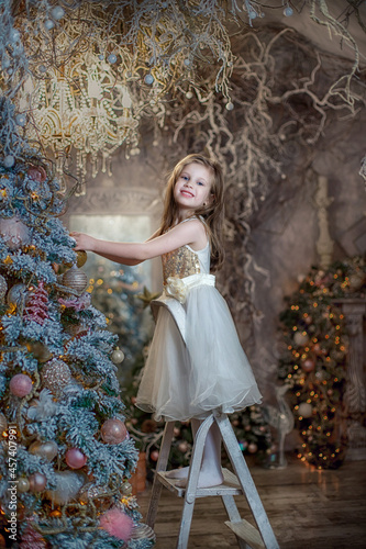 A girl standing on a ladder on a ladder dresses up a Christmas tree.
