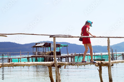 Fototapeta Naklejka Na Ścianę i Meble -  A girl in a red T-shirt walks along a fishing pier