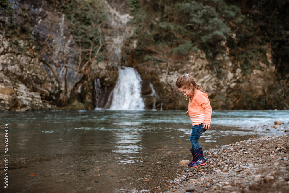Small girl paddles by river in front of waterfall Small girl paddles by river in front of waterfall