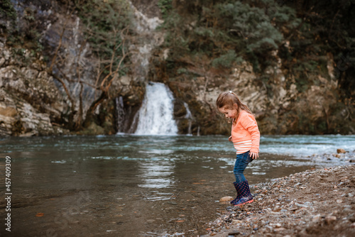 Small girl paddles by river in front of waterfall © Cavan