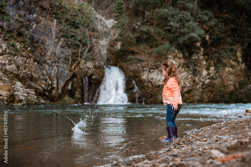 Girl throws stone into river in front of waterfall