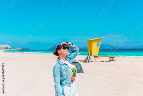 Young woman in sunglasses is smiling and looking to the sun on a beach photo