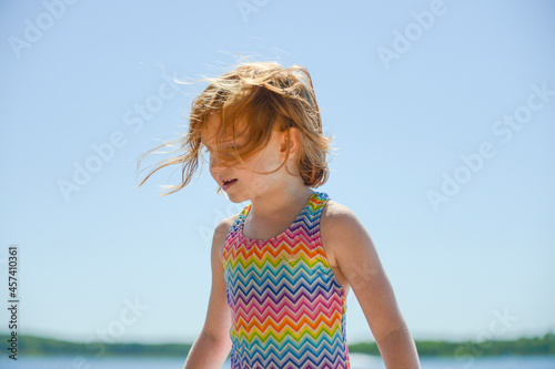 Happy little redhead girl in swimsuit, wind blowing her hair. photo