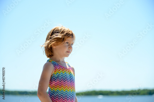Little redhead girl in swimsuit by a lake. photo