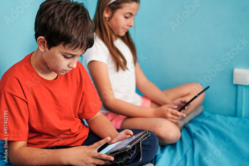 Boy and girl sitting on bed looking at tablet in room at home