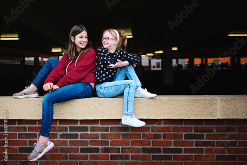 Two happy tween girls sitting on a brick wall together talking. photo