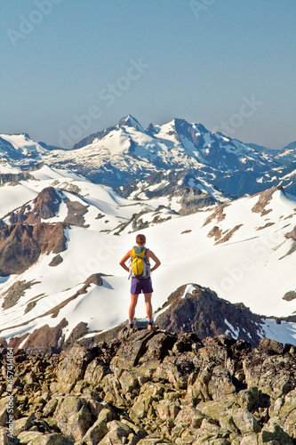 Rear view of attractive fit woman on mountain summit wearing backpack.