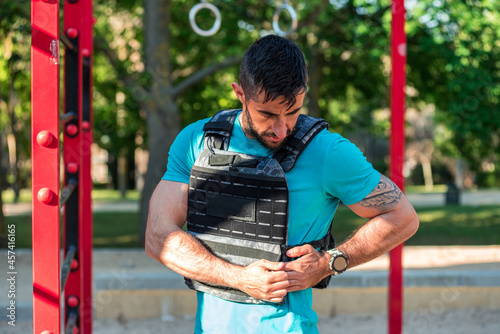 Dark-haired man with beard adjusting a weight vest in a fitness park. Outdoor fitness concept. photo