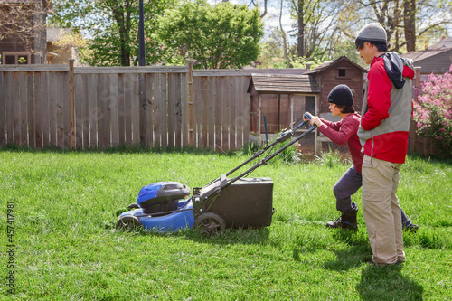 A boy mows lawn in early spring while father watches over him