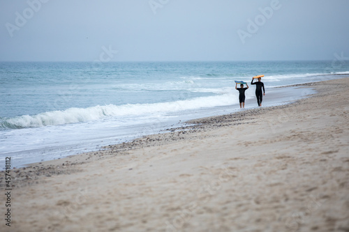 mother and son in distance walking down beach carrying boogie boards photo