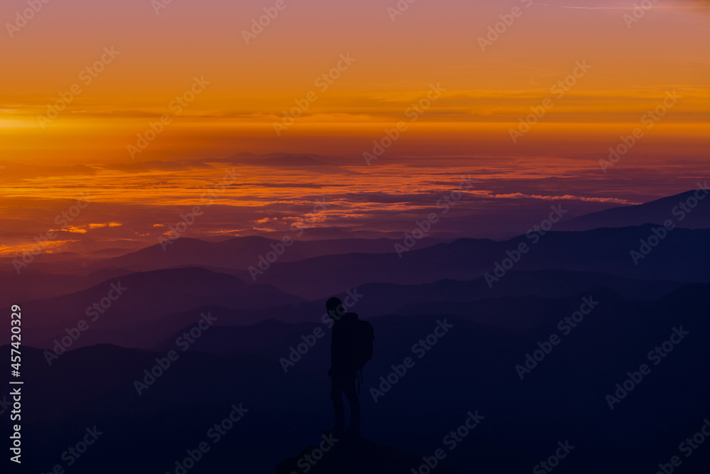 A man standing on top of a mountain as the sun sets. Goals and achievements concept photo composite.