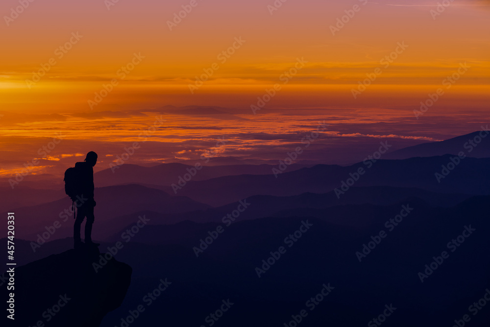 A man standing on top of a mountain as the sun sets. Goals and achievements concept photo composite.