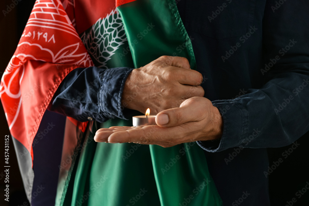 Man with flag of Afghanistan and candle on dark background, closeup