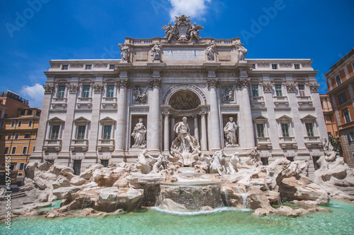 Daytime front view photo of the Trevi Fountain (Fontana di Trevi) in Rome, Italy with a blue sky.