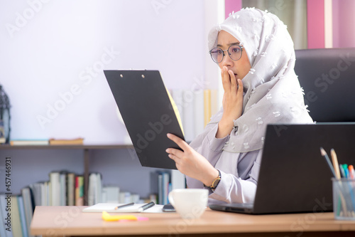 An Asian Muslim office worker is sitting in front of a laptop computer at his desk and is shocked by the results of his office files at the office.