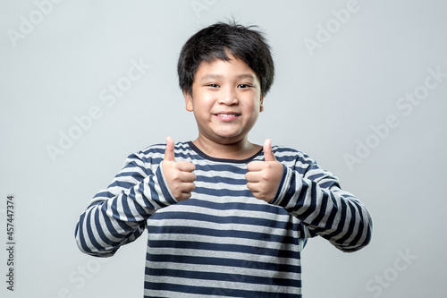 Portrait of a cute Asian boy smiling and showing thumbs up gesture on white background.