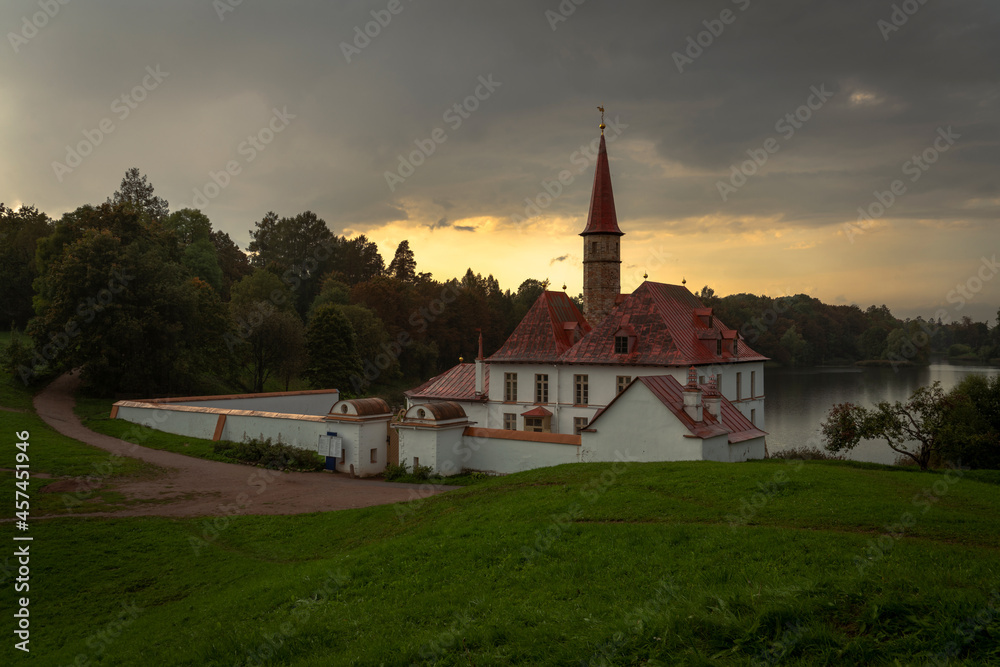 View of the Priory Palace on the shore of the Black Lake against the background of the sunset sky on an autumn evening, Gatchina, St. Petersburg, Russia