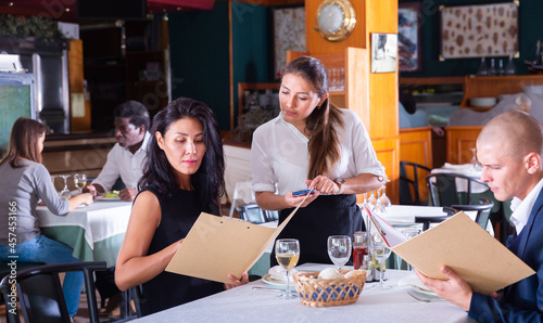 smiling female waiter taking order from adult man and woman in restaurante