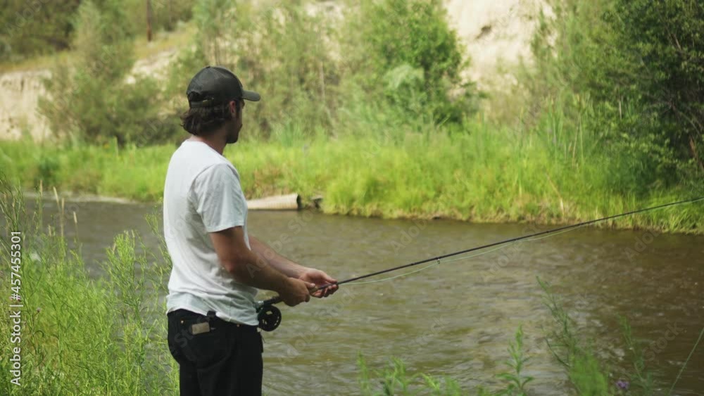 Caucasian man fly fishing in fast-flowing river, lush green river bank Caucasian man fly fishing in fast-flowing river, lush green river bank
