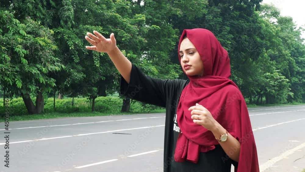 Slow motion of a young smiling Afghan girl in hijab in a black and red dress standing on the side of the road waiting for public transport to go back home. Concept of tree in the background,Afghan.