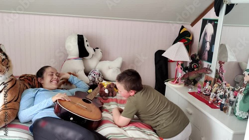 Mother playing guitar together with autistic son - Mother laying on bed interacting with happy boy - Tiptoeing and hand flapping stereotypic movements photo
