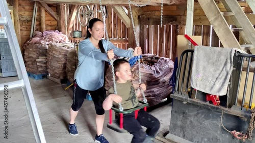 Mom pushing autistic son in swing inside barn - Having a good time together - Boy flapping doing stereoptypic movements like hand flapping when laughing photo