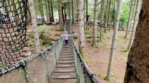 Cute young blonde girl waking on rope suspension bridge inside woods of Mikkelparken theme park - Norway photo