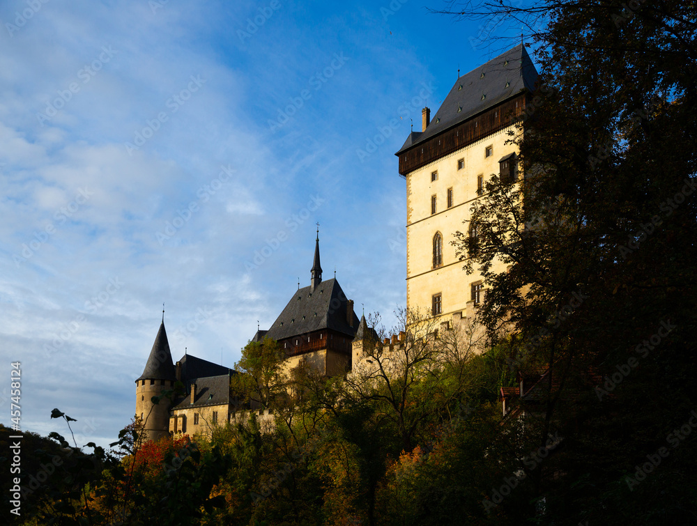 View of large Gothic Karlstejn Castle on top of hill on sunny autumn day, Czech Republic..