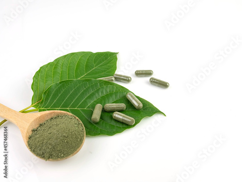 Kratom leaves and powder on spoon with capsule, isolated on white background.
