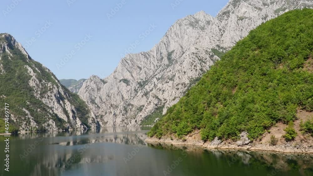 Beautiful alpine mountains reflecting on calm water of lake in Northern Albania