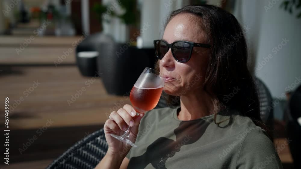 a happy successful lady in sunglasses is sitting on the veranda of a restaurant and drinking a glass of cold pink champagne a happy successful lady in sunglasses is sitting on the veranda of a restaurant and drinking a glass of cold pink champagne