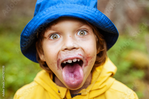 A cute boy shows his tongue lilac from blueberries. Portrait of a child in the forest.