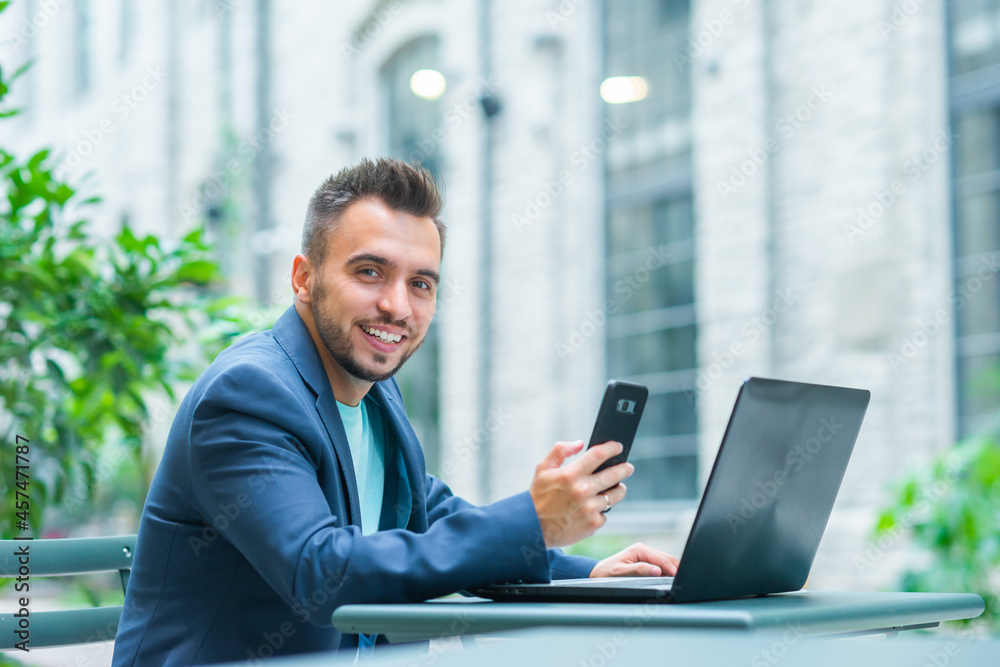 Young successful caucasian businessman works in an outdoor cafe using a computer. Business, freelance and remote work. Young successful caucasian businessman works in an outdoor cafe using a computer. Business, freelance and remote work.