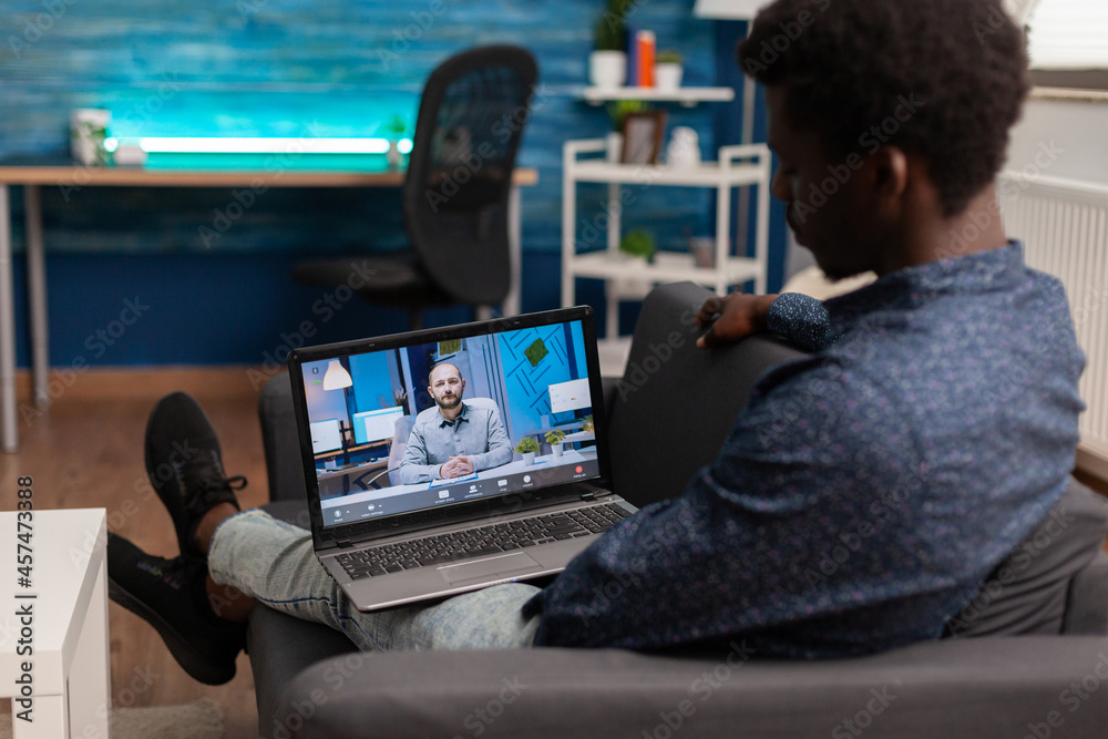African american student having online management school webinar on laptop during coronavirus lockdown in living room. Videocall meeting teleconference telwork on laptop. Computer user
