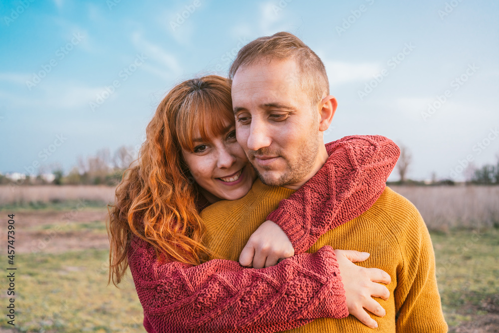 Young happy couple wearing warm blouses standing in the field under a blue sky Young happy couple wearing warm blouses standing in the field under a blue sky