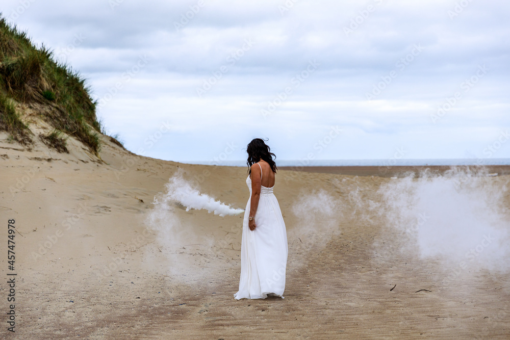 Junge schöne Frau im Hochzeitskleid am Strand mit einer Rauchfackel und weißen Rauch Junge schöne Frau im Hochzeitskleid am Strand mit einer Rauchfackel und weißen Rauch