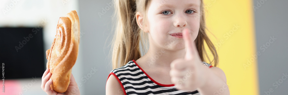 Little girl eating delicious sweet bun and showing thumb up Little girl eating delicious sweet bun and showing thumb up